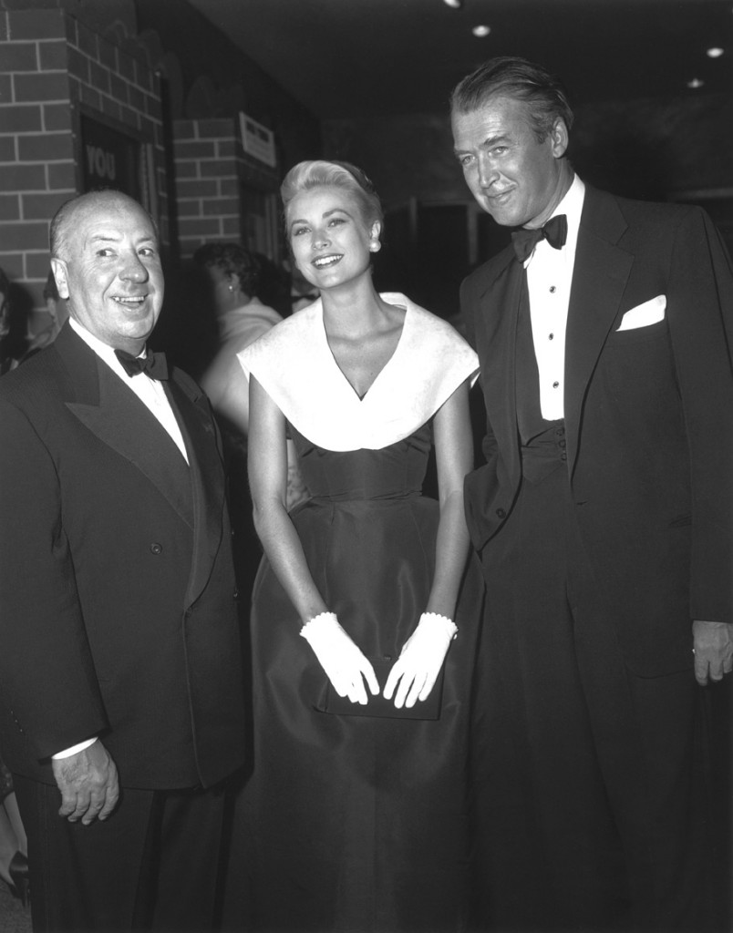 Grace Kelly in Christian Dior New York, surrounded by Alfred Hitchcock and James Stewart at the premiere of Rear Window in 1954. © Paramount/The Kobal Collection.